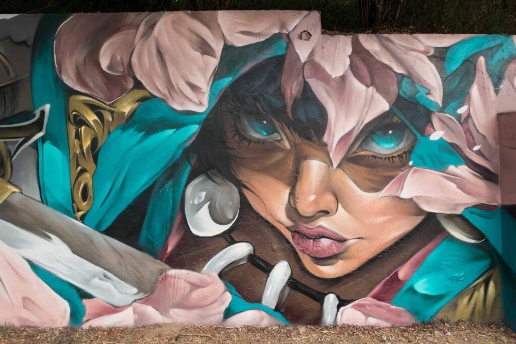 Detalle del mural Beware: rostro con capucha turquesa, collar de colmillos y un pétalo rosa sobre un ojo