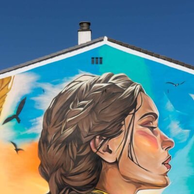 Mural de Santa Casilda en Briviesca: rostro de perfil con trenza sobre cielo azul en la medianera de un edificio