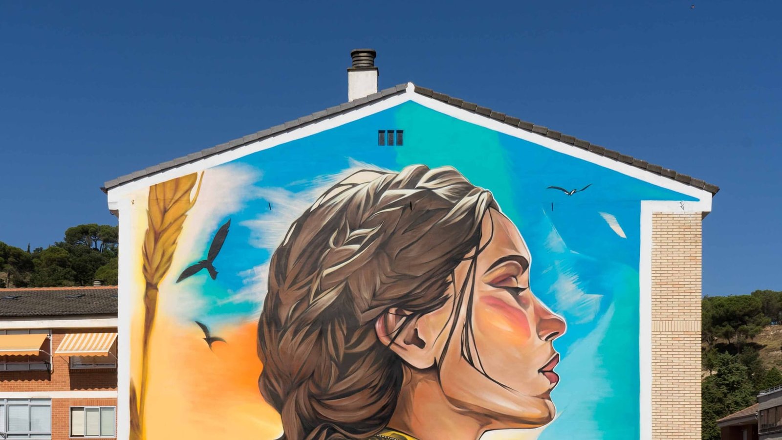 Mural de Santa Casilda en Briviesca: rostro de perfil con trenza sobre cielo azul en la medianera de un edificio