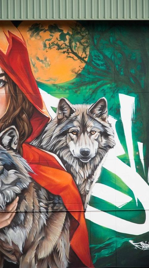 Detalle lateral del mural escolar con lobo y fondo verde durante el proceso de ejecución