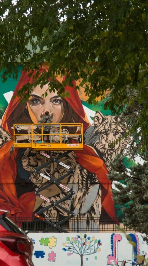 Proceso de pintura de mural escolar con elevadora en fachada de colegio en Madrid