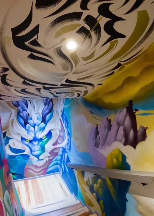 Graffiti interior con retratos y dragón en escalera de acceso a bodega