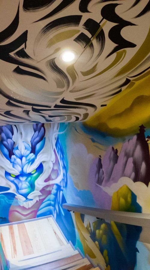 Graffiti interior con retratos y dragón en escalera de acceso a bodega