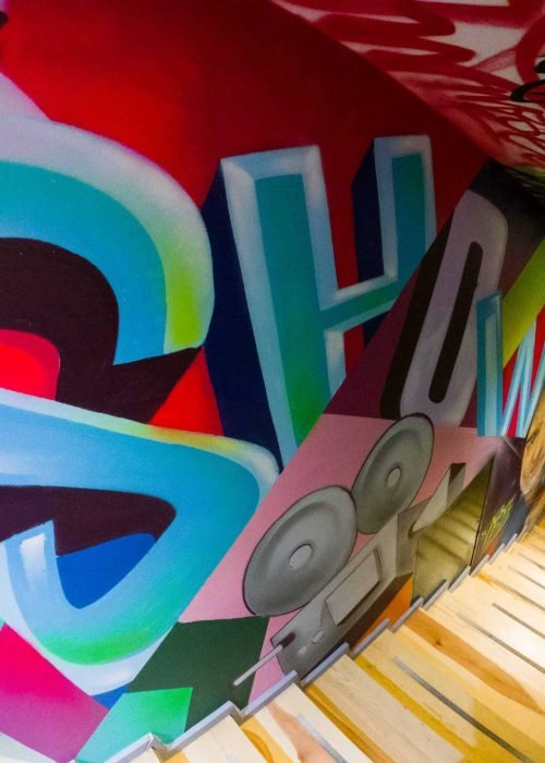 Graffiti interior con retratos y dragón en escalera de acceso a bodega