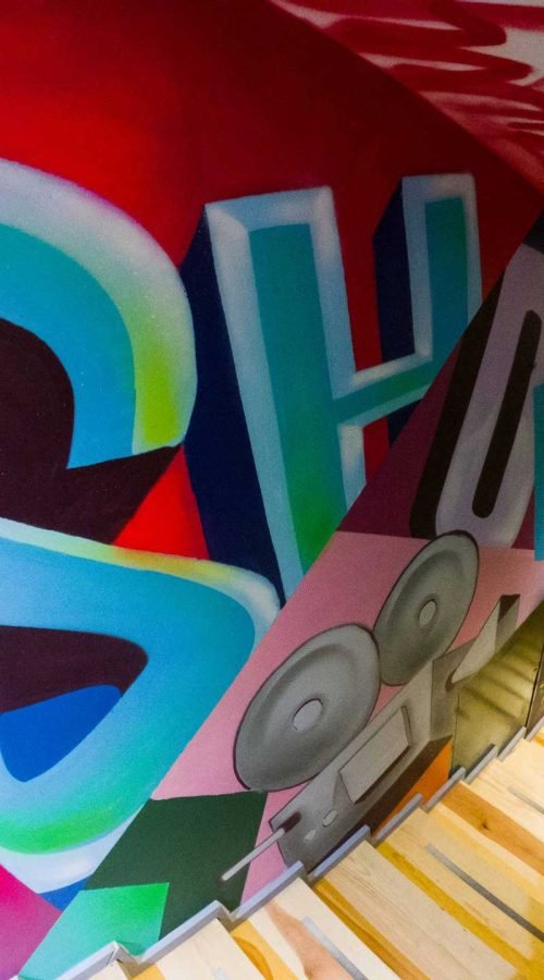 Graffiti interior con retratos y dragón en escalera de acceso a bodega