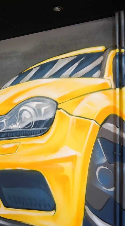 Mural con coche BMW amarillo en fachada de Autoescuela Gala Metropolitano