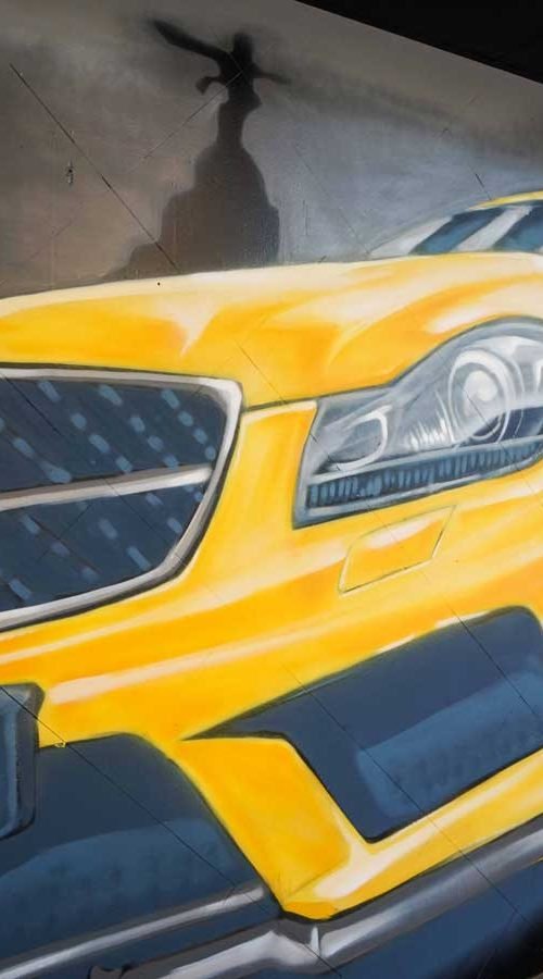 Mural con coche BMW amarillo en fachada de Autoescuela Gala Metropolitano