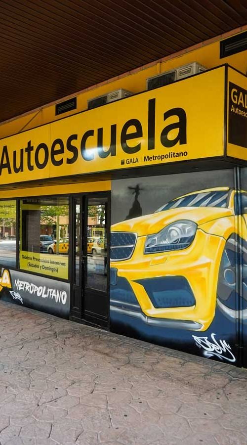 Mural con coche BMW amarillo en fachada de Autoescuela Gala Metropolitano