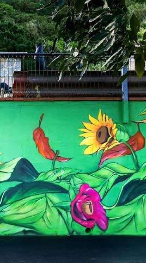 Fragmento del mural con flores, hojas tropicales y colores vivos en el exterior del hotel