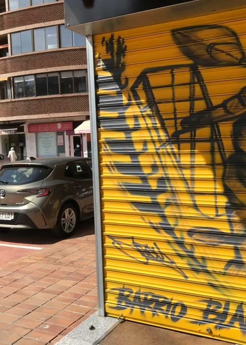 Mural con moto de carreras en cierre metálico del Barrio Blanco (Madrid), estilo urbano