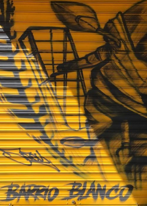 Mural con moto de carreras en cierre metálico del Barrio Blanco (Madrid), estilo urbano