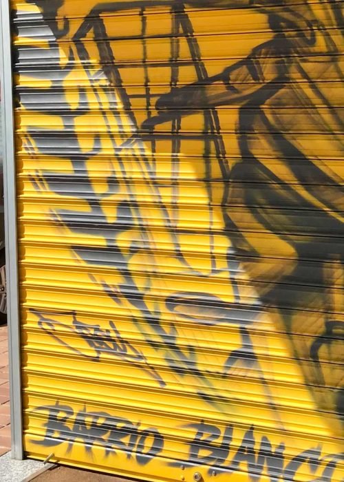 Mural con moto de carreras en cierre metálico del Barrio Blanco (Madrid), estilo urbano