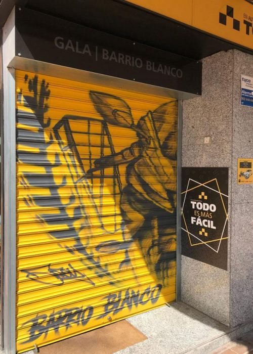 Mural con moto de carreras en cierre metálico del Barrio Blanco (Madrid), estilo urbano