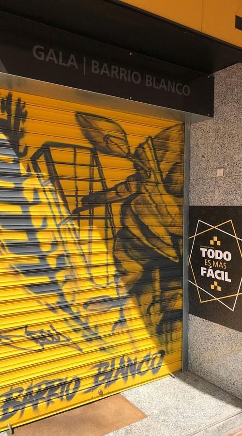 Mural con moto de carreras en cierre metálico del Barrio Blanco (Madrid), estilo urbano