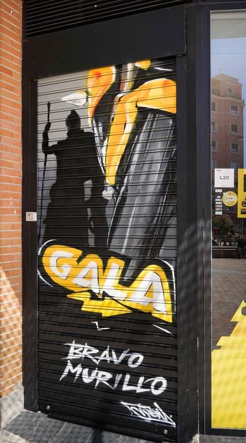 Moto deportiva amarilla y silueta urbana en mural para Gala Bravo Murillo, Madrid