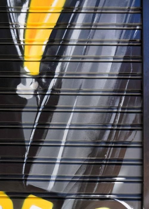 Moto deportiva amarilla y silueta urbana en mural para Gala Bravo Murillo, Madrid