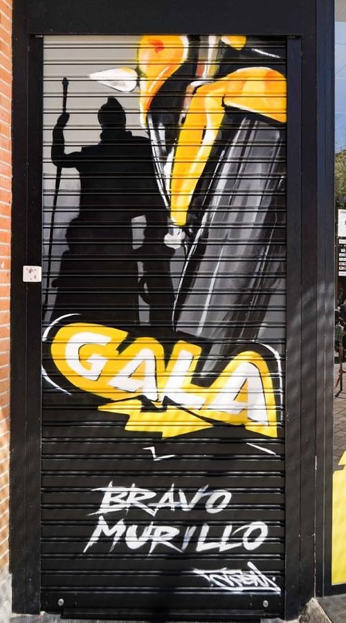 Moto deportiva amarilla y silueta urbana en mural para Gala Bravo Murillo, Madrid