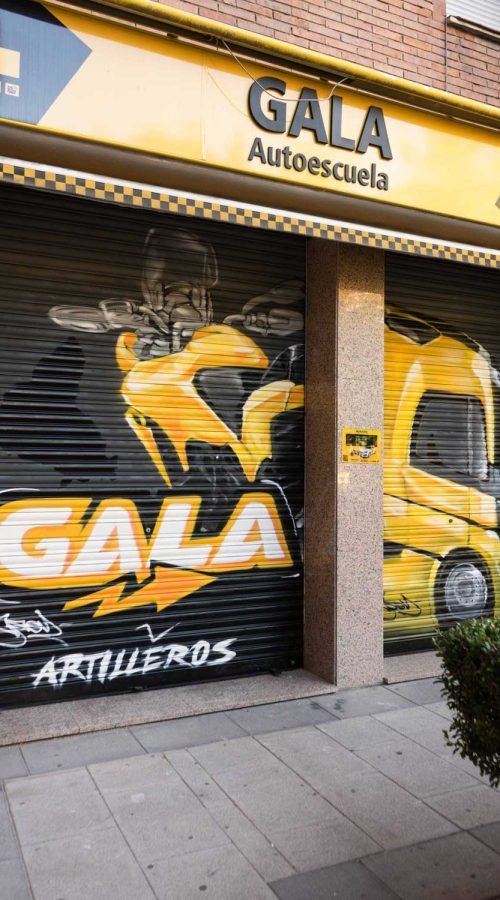 Cierre pintado de Autoescuela Gala con camión y moto en estilo urbano
