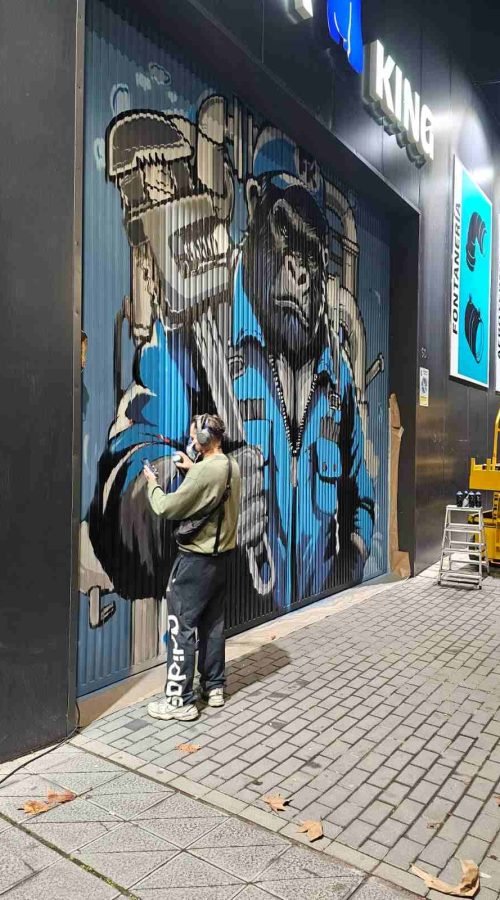 Proceso de mural en puerta industrial de Fontaking con artista pintando el gorila fontanero