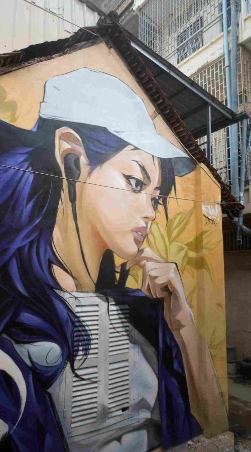 Mural graffiti en fachada de Camboya, retrato femenino con gorra para S’art Urban Art Festival.