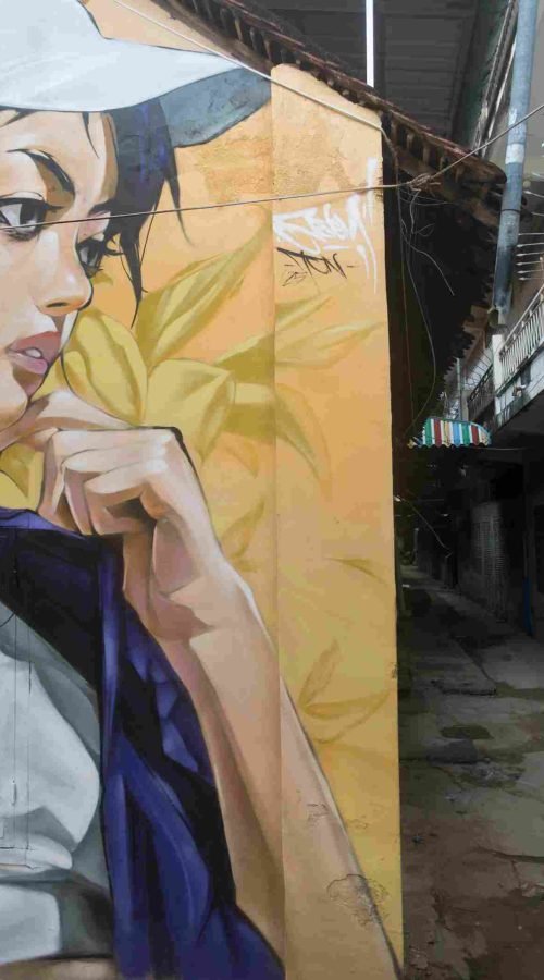 Mural graffiti en fachada de Camboya, retrato femenino con gorra para S’art Urban Art Festival.