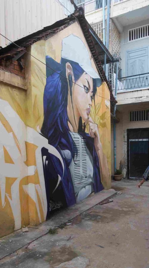 Mural graffiti en fachada de Camboya, retrato femenino con gorra para S’art Urban Art Festival.