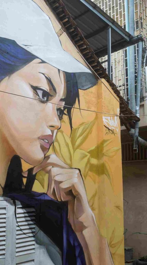 Mural graffiti en fachada de Camboya, retrato femenino con gorra para S’art Urban Art Festival.