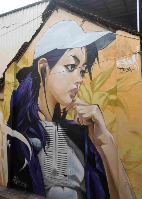 Mural graffiti en fachada de Camboya, retrato femenino con gorra para S’art Urban Art Festival.
