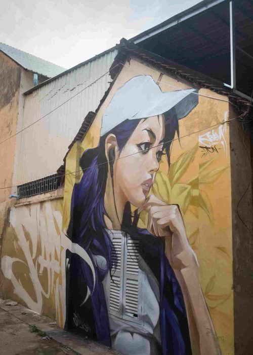 Mural graffiti en fachada de Camboya, retrato femenino con gorra para S’art Urban Art Festival.