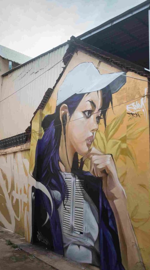 Mural graffiti en fachada de Camboya, retrato femenino con gorra para S’art Urban Art Festival.
