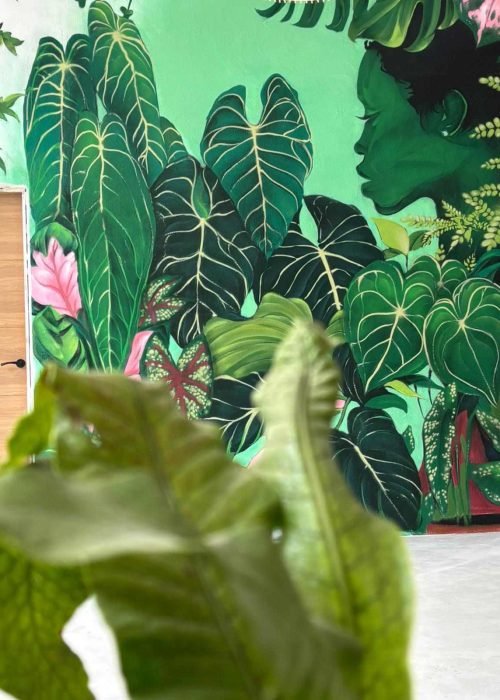 Mural vegetal en tienda Plantukas de Torrelavega con hojas tropicales y retrato femenino entre vegetación