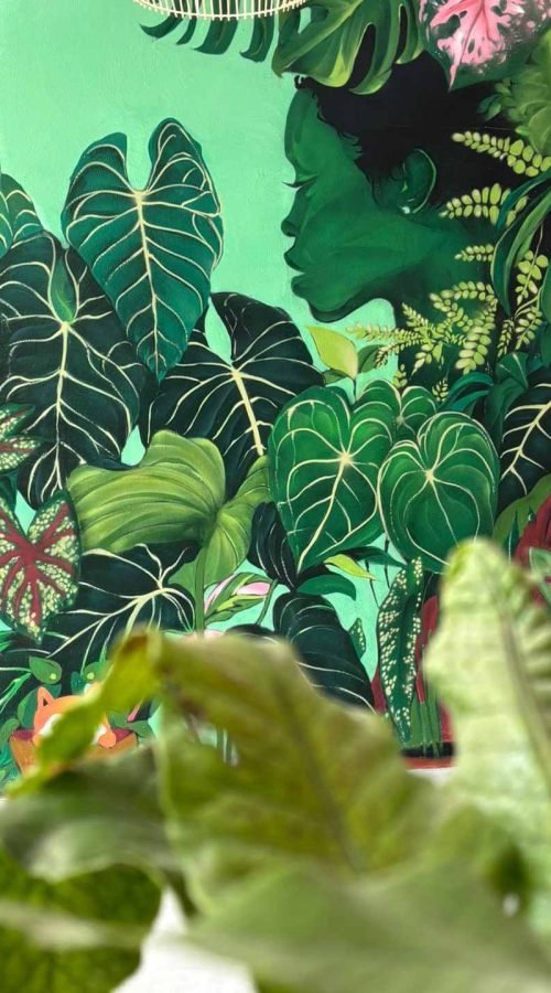 Mural graffiti de plantas en Cantabria con follaje tropical y perfil femenino en interior comercial