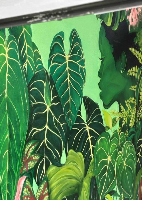 Detalle de mural vegetal en Torrelavega visto entre puertas negras con perfil femenino y hojas tropicales