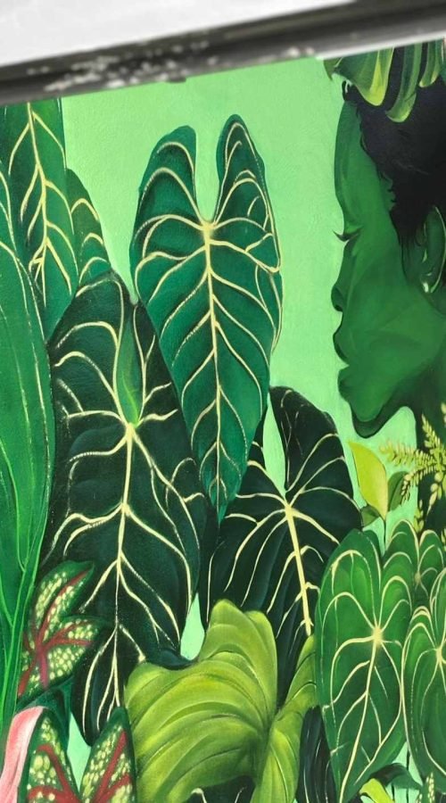 Detalle de mural vegetal en Torrelavega visto entre puertas negras con perfil femenino y hojas tropicales
