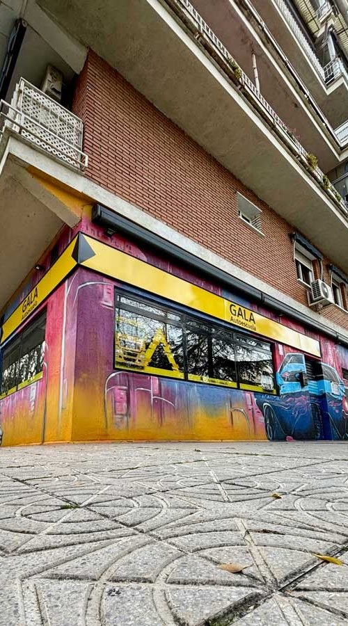 Mural con coches y motos en fachada de Autoescuelas Gala en Móstoles